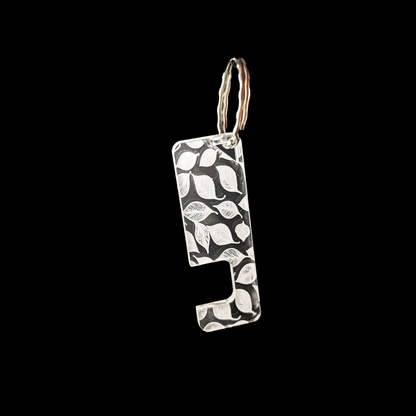 a transparent phone stand key ring with an engraved falling leaf texture against a black background. Rua phone stand by Fiach Rua