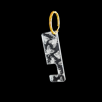 a transparent phone stand key ring with an engraved Fly texture against a black background. Rua phone stand by Fiach Rua