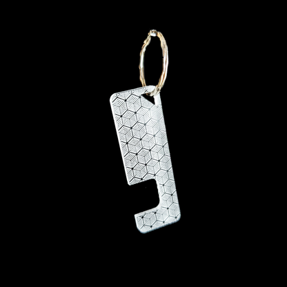 a transparent phone stand key ring with an engraved geometric cube texture against a black background. Rua phone stand by Fiach Rua